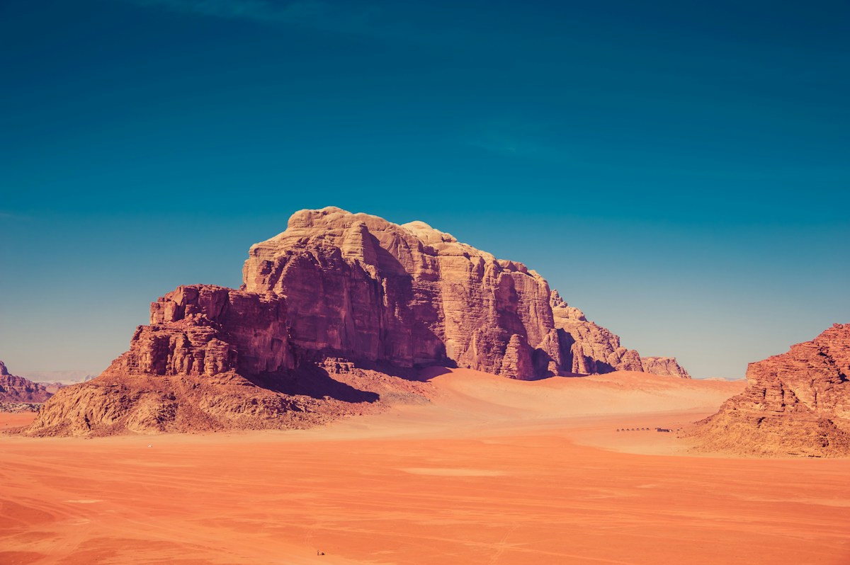 Brązowe formacje skalne otoczone czerwonym piaskiem Wadi Rum